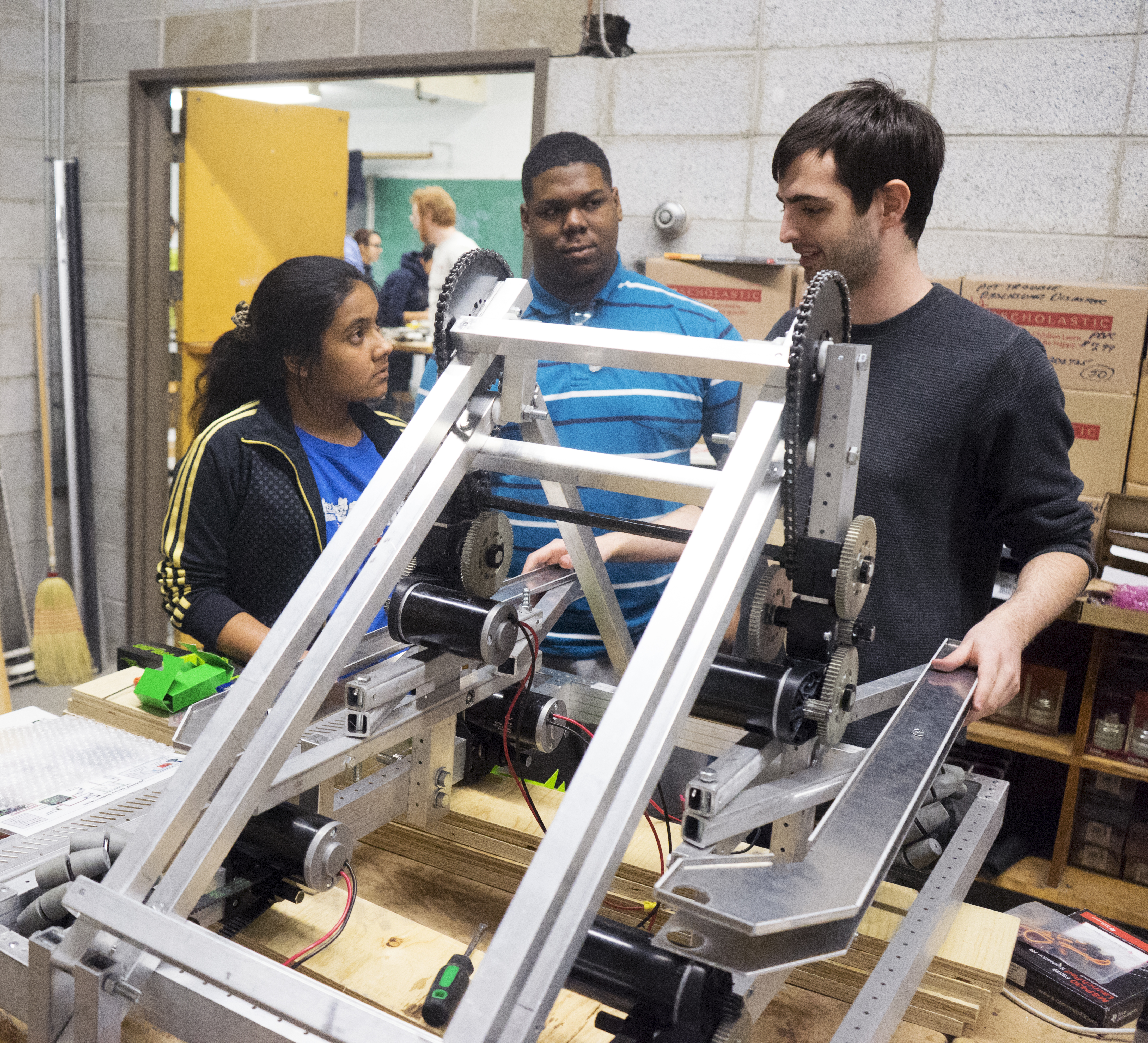 Robotics mentor and two students having a conversation behind a half-built robot frame.  